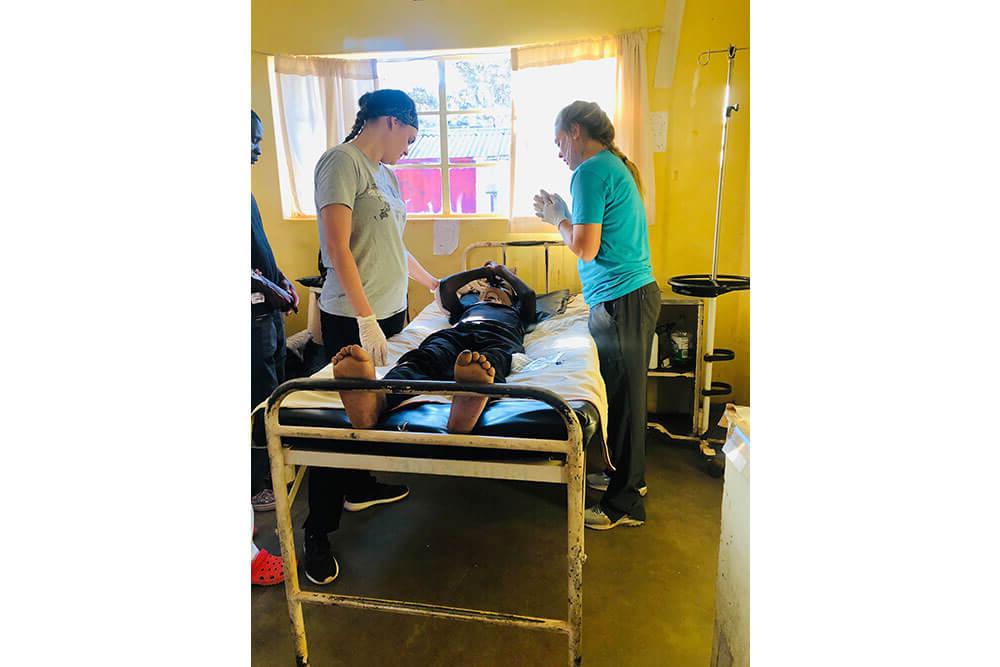 两名女理疗专业的学生站在病人的病床两旁