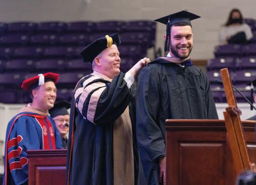 male graduate receives hood from professor during commencement ceremony